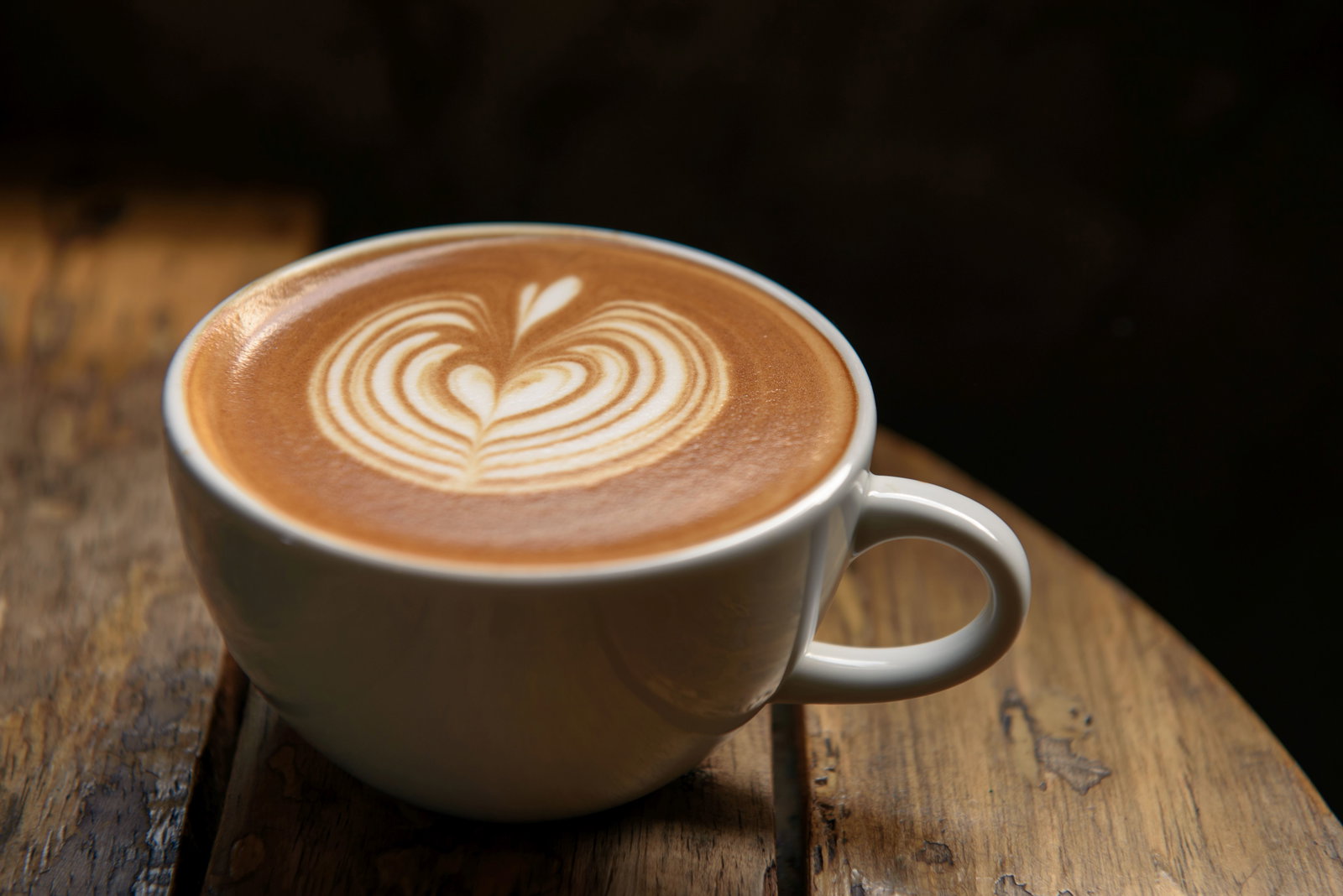 Eine Tasse Kaffee mit Milchschaum in Herzform steht auf einem Holztisch.