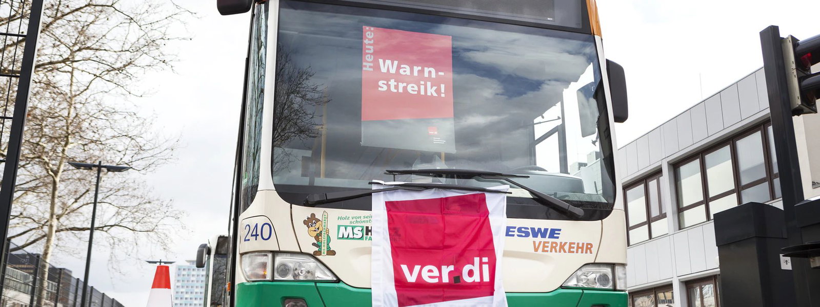 Ein Linienbus steht auf einer Straße. Am Scheibenwischer hängt eine rot weiße Flagge mit der Aufschrift Verdi. In der Frontscheibe hängt ein rotes Schild mit dem Hinweis Warnstreik.