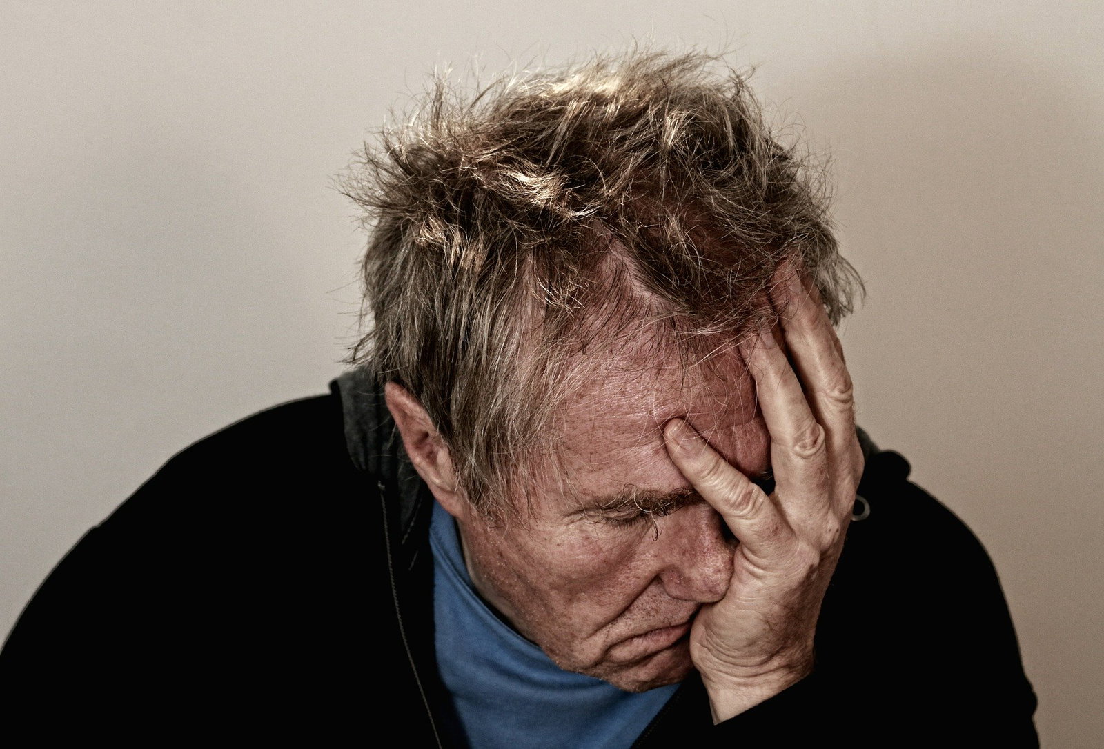 Älterer Mann fasst sich an den Kopf. Die Augen sind geschlossen und sein Haar zerzaust.